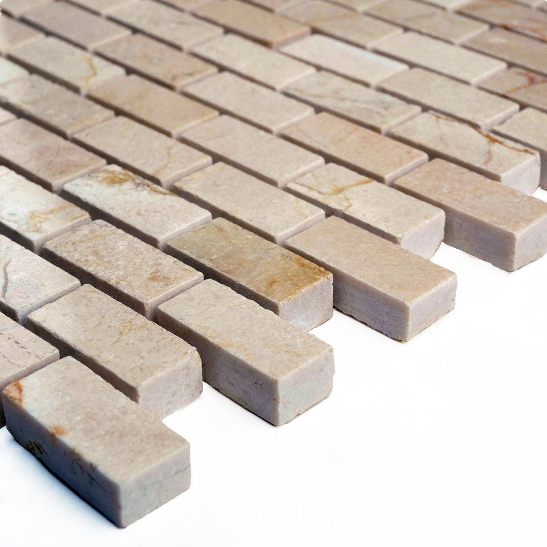 Polished 5/8 by 1 1/4 Crema Marfil marble brick mosaic photographed from an angle, reflecting soft light across the uniform creamy tilework.