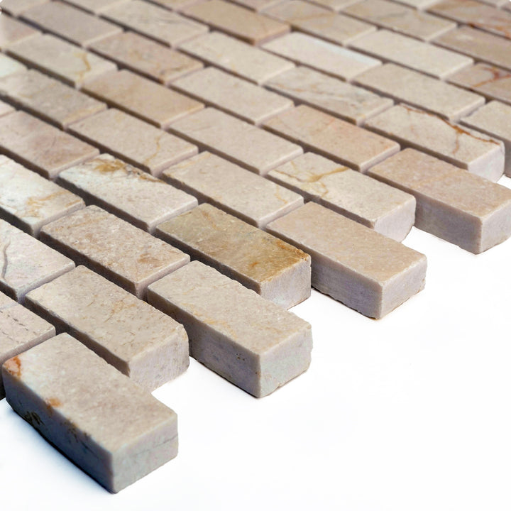 Polished 5/8 by 1 1/4 Crema Marfil marble brick mosaic photographed from an angle, reflecting soft light across the uniform creamy tilework.