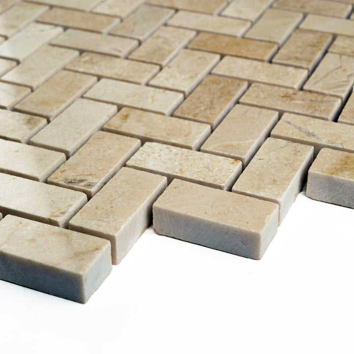 5/8 by 1 1/4 herringbone mosaic in honed Crema Marfil marble, viewed at an angle to emphasize the subtle zigzag texture and satin surface.