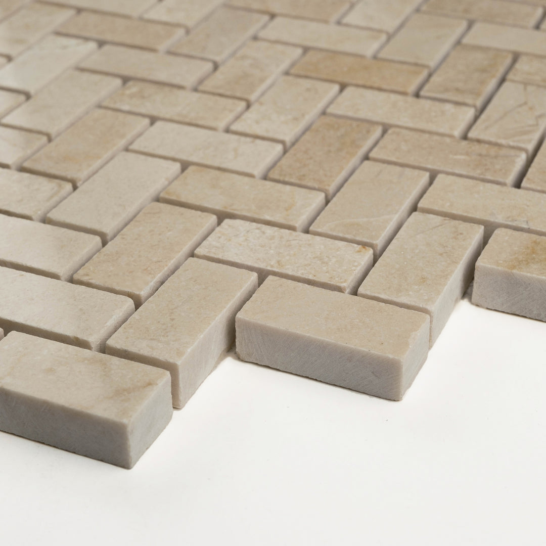 Polished 5/8 by 1 1/4 herringbone Crema Marfil marble mosaic shown corner-on, with a dynamic V-pattern and refined shine.