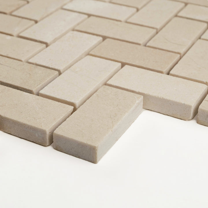 1x2 herringbone mosaic in honed Crema Marfil marble from a corner view, capturing the soft creamy texture and classic angular flow.