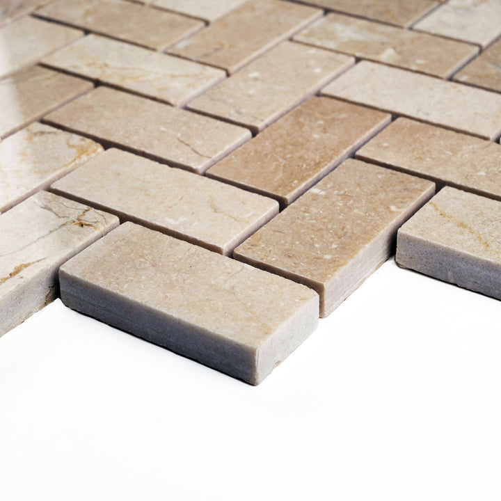 Corner shot of polished 1x2 herringbone Crema Marfil mosaic, featuring reflective surfaces and neutral warmth in a tight V-shaped layout.