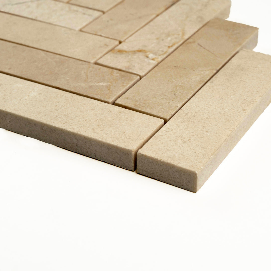 Honed 1x4 herringbone Crema Marfil marble mosaic viewed at an angle, emphasizing linear sophistication with a soft, natural finish.