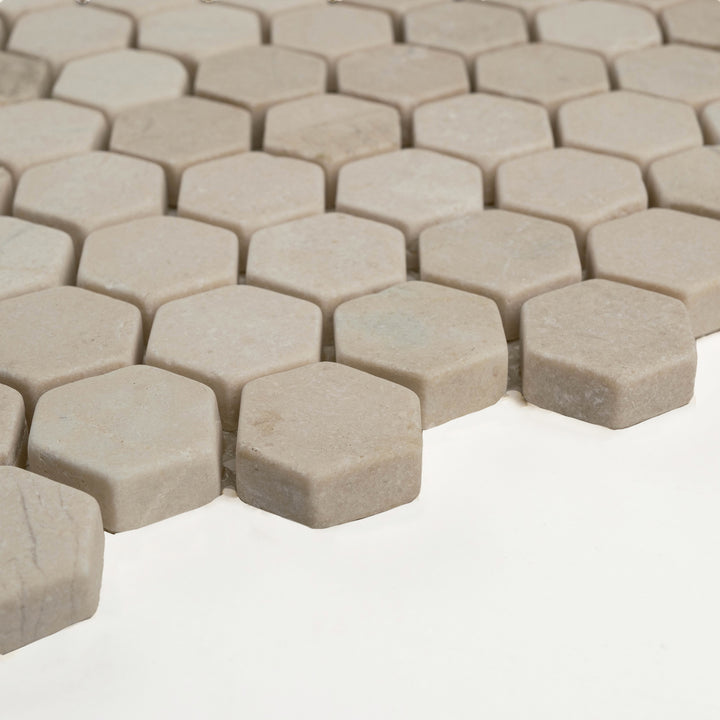 Corner-shot of 1 inch tumbled hexagon Crema Marfil marble mosaic, with softened edges and a rustic, timeworn appearance.
