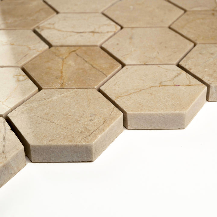 Polished 2 inch hexagon Crema Marfil mosaic viewed from a corner, highlighting its glossy sheen and symmetrical geometric pattern.
