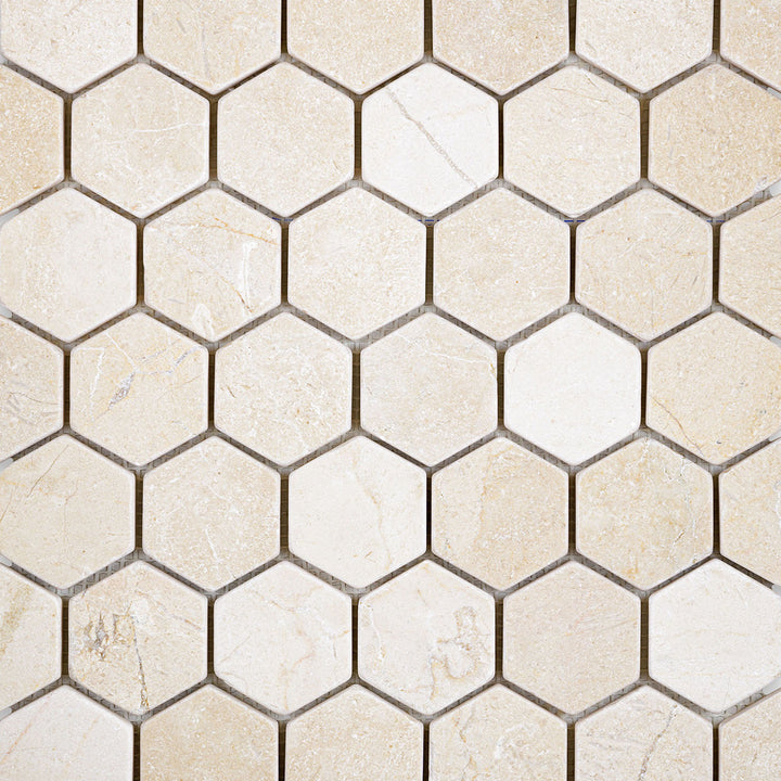 Tumbled 2" hexagon mosaic of Crema Marfil Marble shown in a rustic overview to highlight natural imperfections.