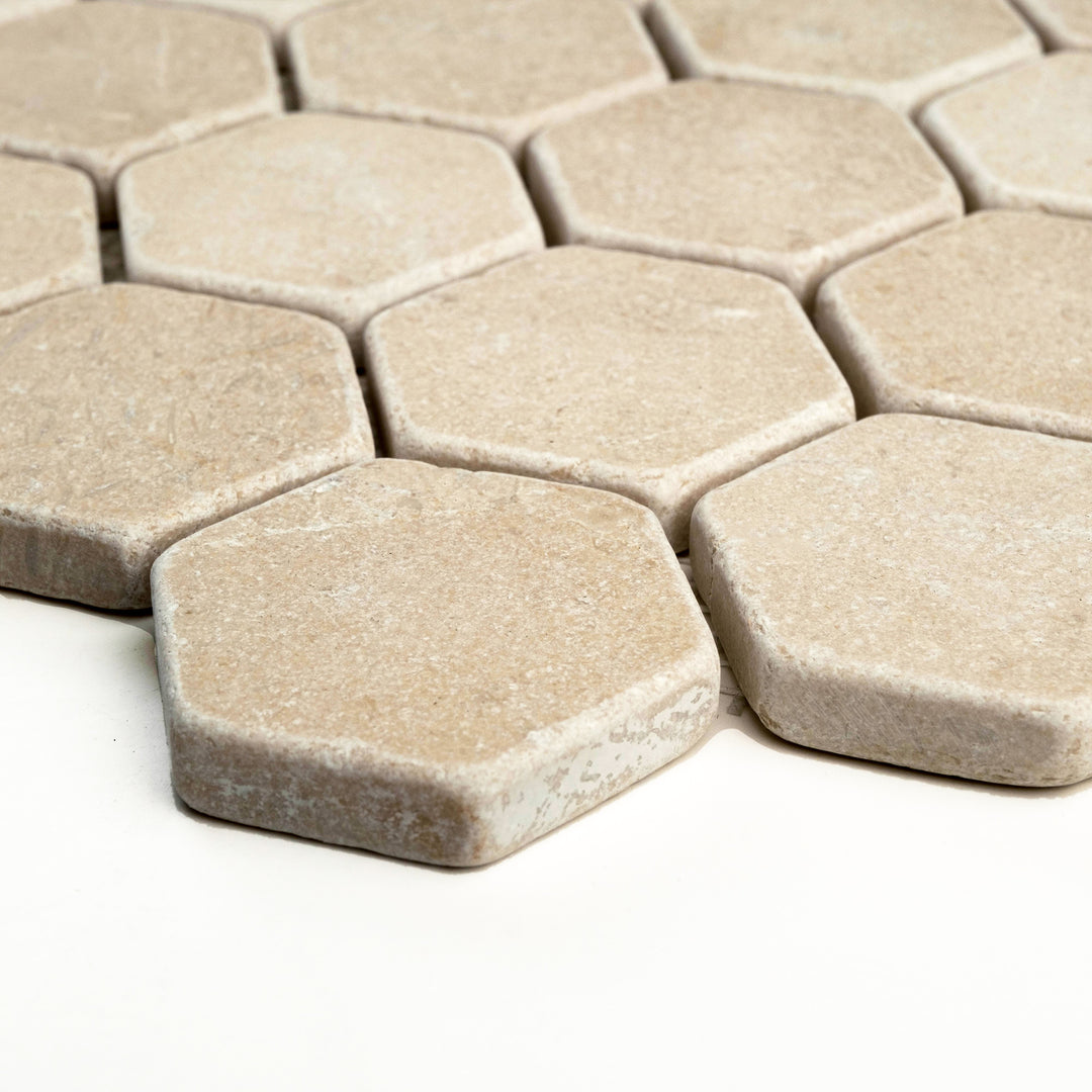 Tumbled 2 inch hexagon Crema Marfil marble mosaic, captured side-on to show its weathered edges and rustic finish in warm beige tones.