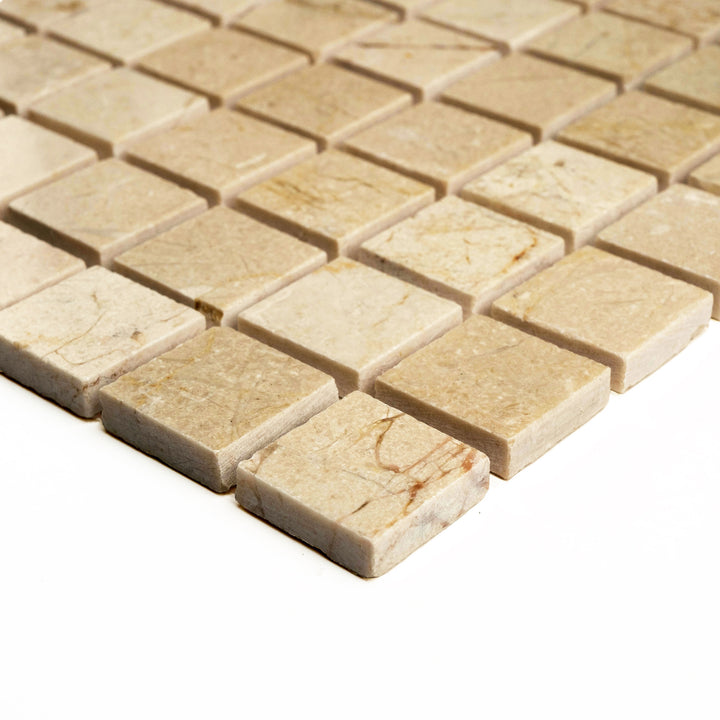 Polished 1 inch square mosaic in Crema Marfil marble, angled to highlight its lustrous finish and precise, modern appeal.