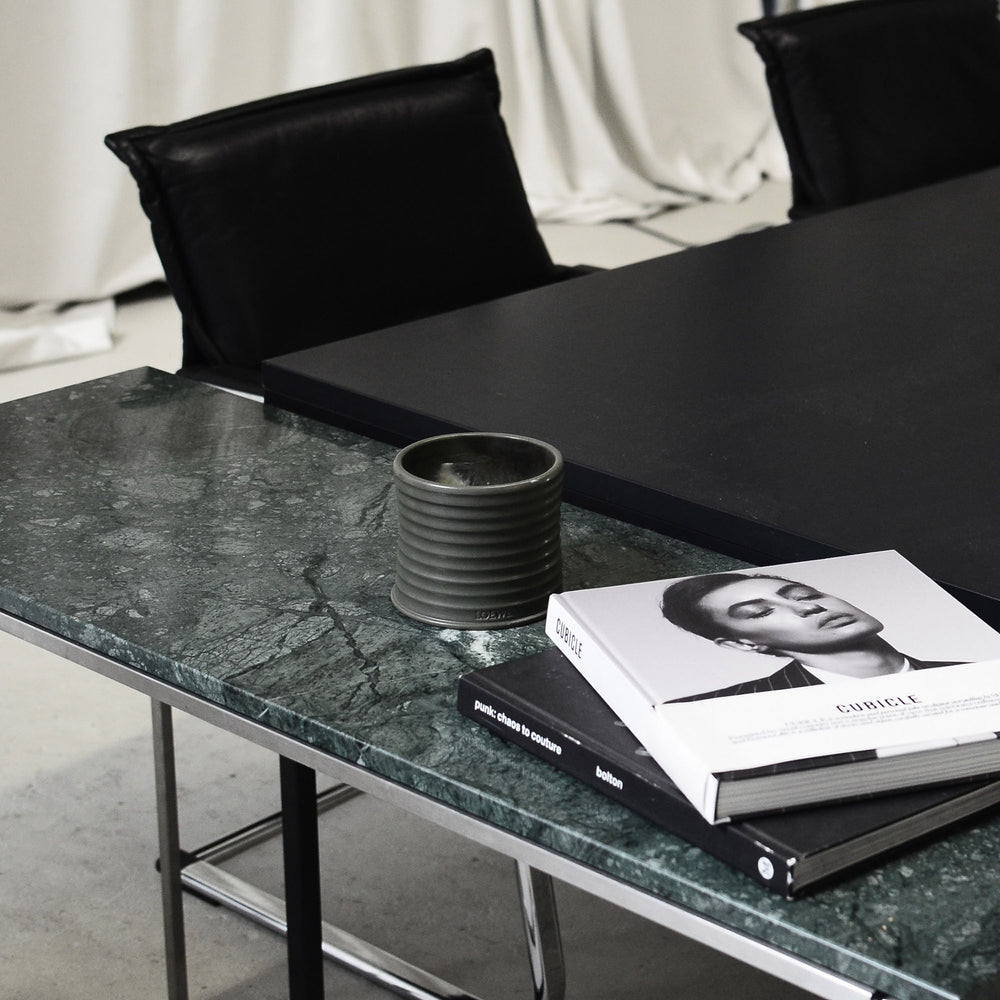 Modern black dining table with marble top, books, and a cup in a minimalistic setting.