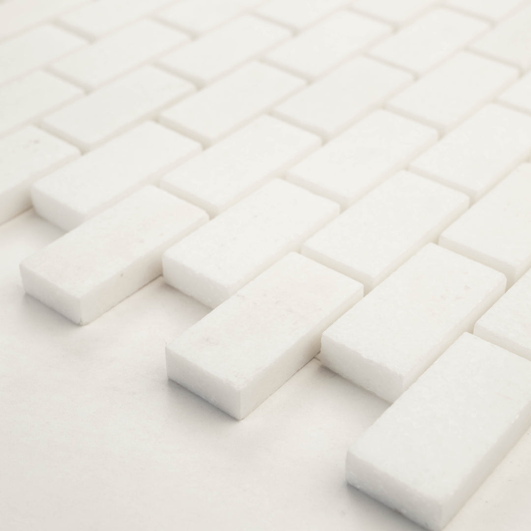 1x2 brick mosaic in honed Thassos White marble, shown at a diagonal angle to bring out its clean grid layout and soft honed surface.