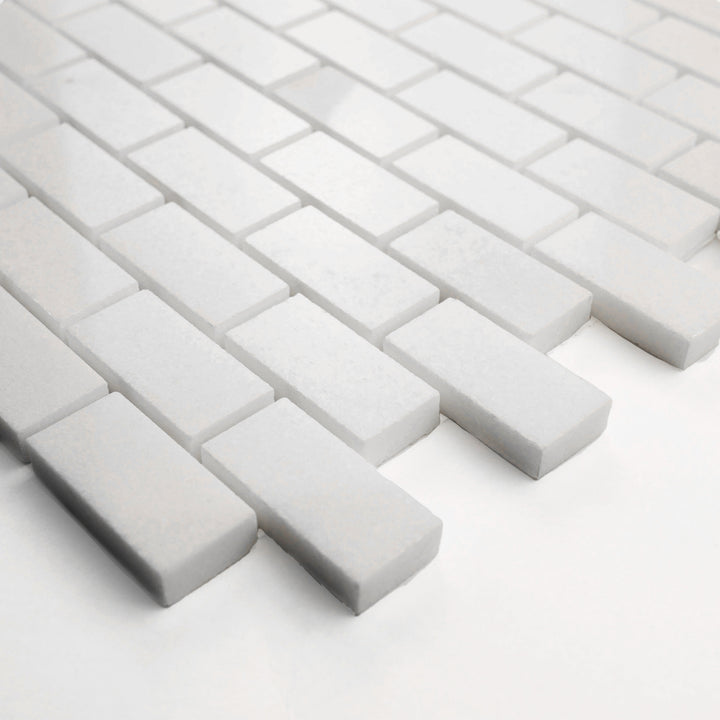 Polished 1x2 brick mosaic in Thassos White marble, corner-shot presentation reveals its elegant shine and precise layout.