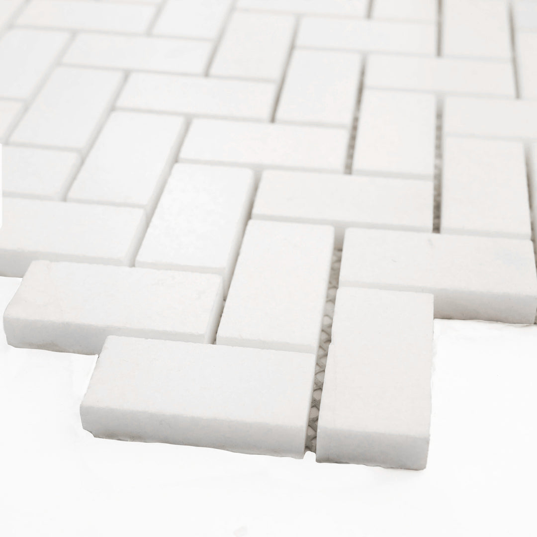 Polished 1x2 herringbone mosaic in Thassos White marble, shown at an angle to showcase sharp angles and radiant polish.