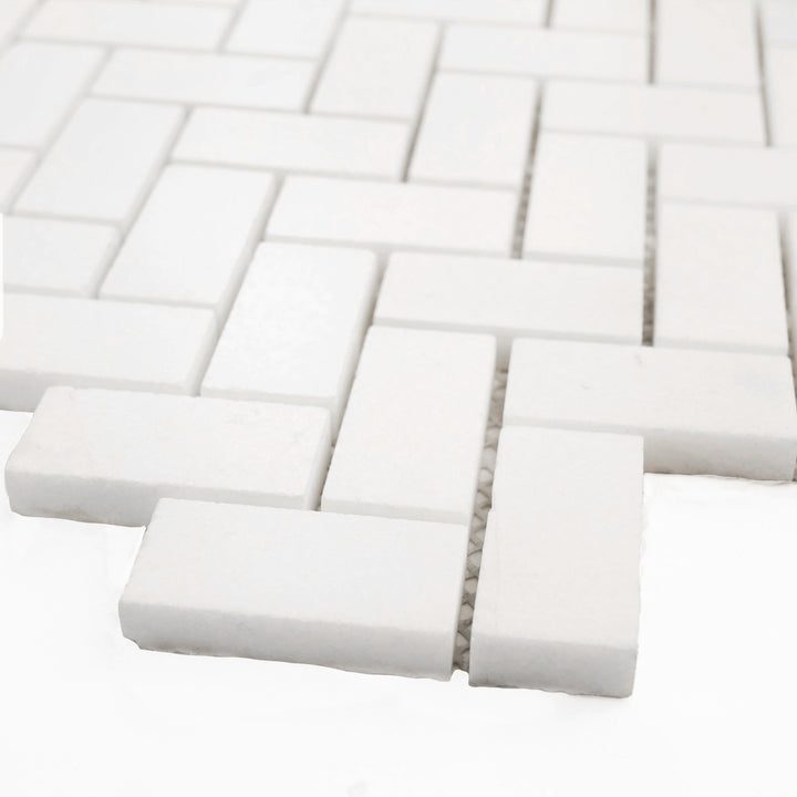 Polished 1x2 herringbone mosaic in Thassos White marble, shown at an angle to showcase sharp angles and radiant polish.