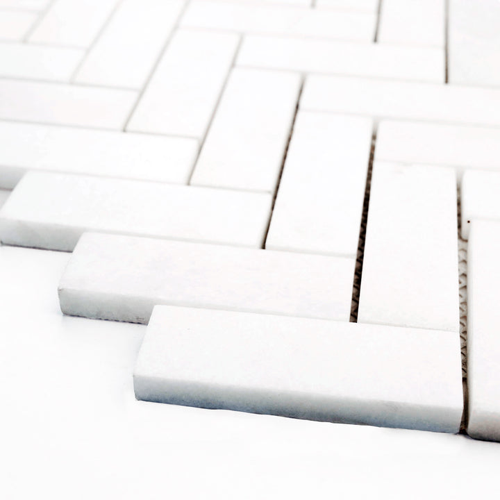 Honed 1x3 herringbone mosaic in Thassos White marble, viewed from the corner to highlight directional flow and soft surface finish.