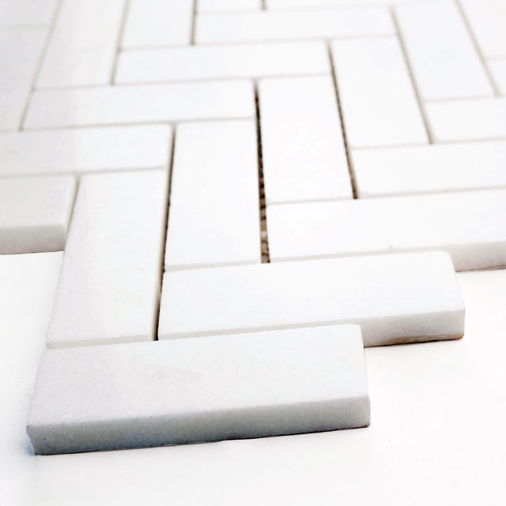 1x3 herringbone polished mosaic in Thassos White marble, angled view brings out elegant shine and distinctive zigzag pattern.