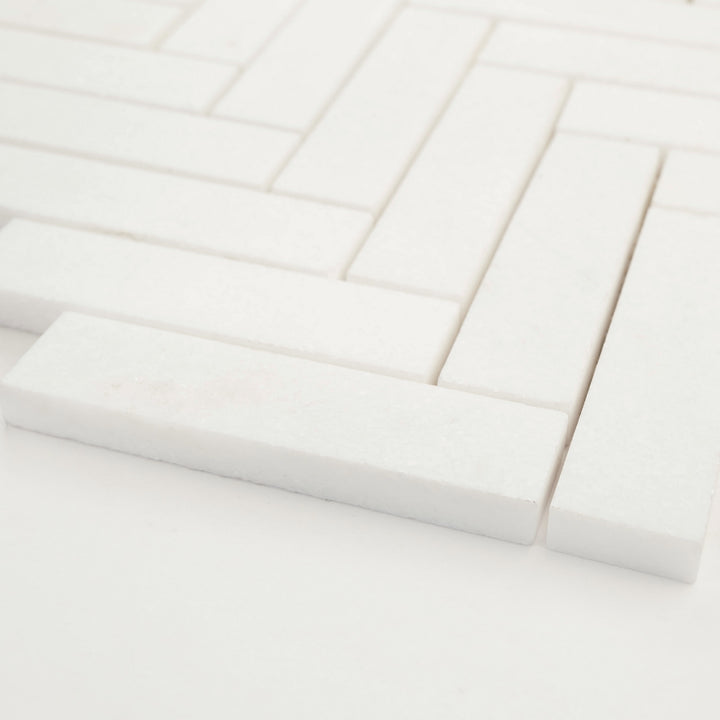 1x4 herringbone mosaic in honed Thassos White marble, shown at a diagonal to showcase the clean lines and natural stone depth.