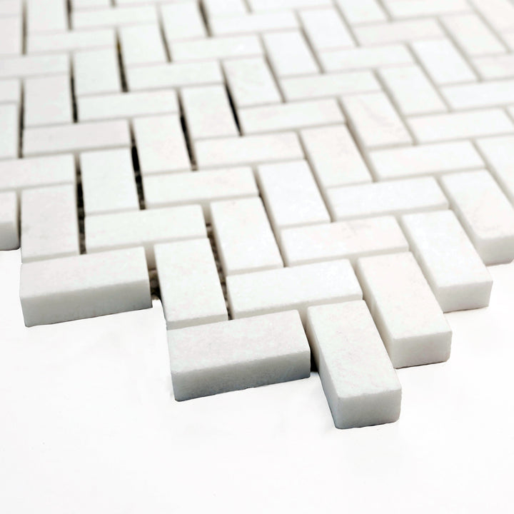 5/8 x 1-1/4 herringbone mosaic in honed Thassos White marble, corner-shot perspective reveals compact layout and matte elegance.