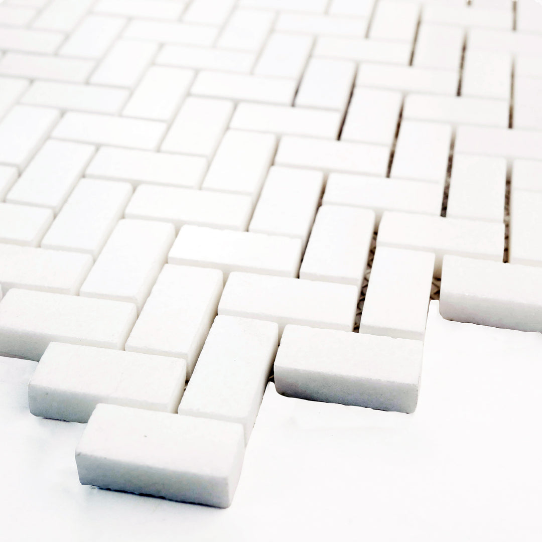 Polished 5/8 x 1-1/4 herringbone mosaic in Thassos White marble, angled view highlights its bright surface and intricate arrangement.