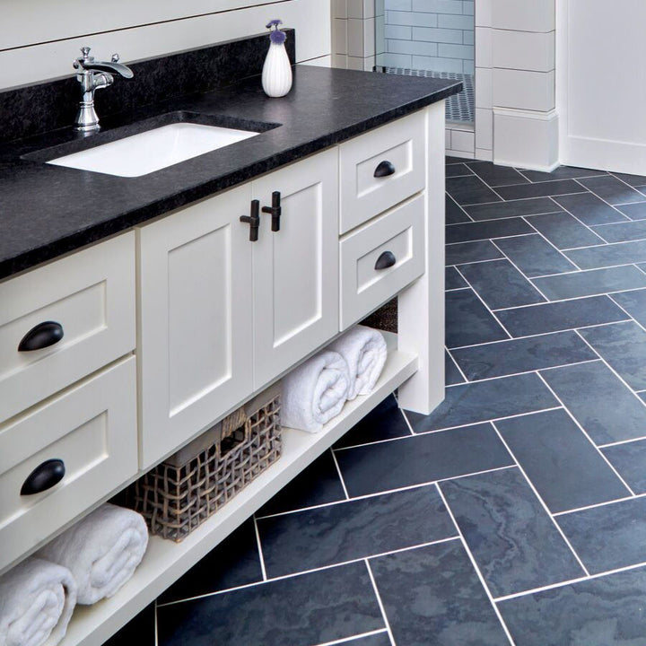 Bathroom vanity with black countertop and white cabinets, featuring a tiled floor.