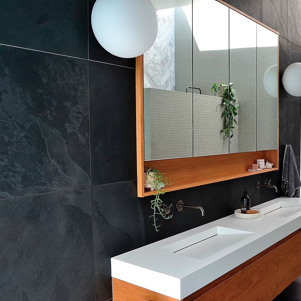 Modern bathroom with dark tiled walls, a white sink, and a large mirror.