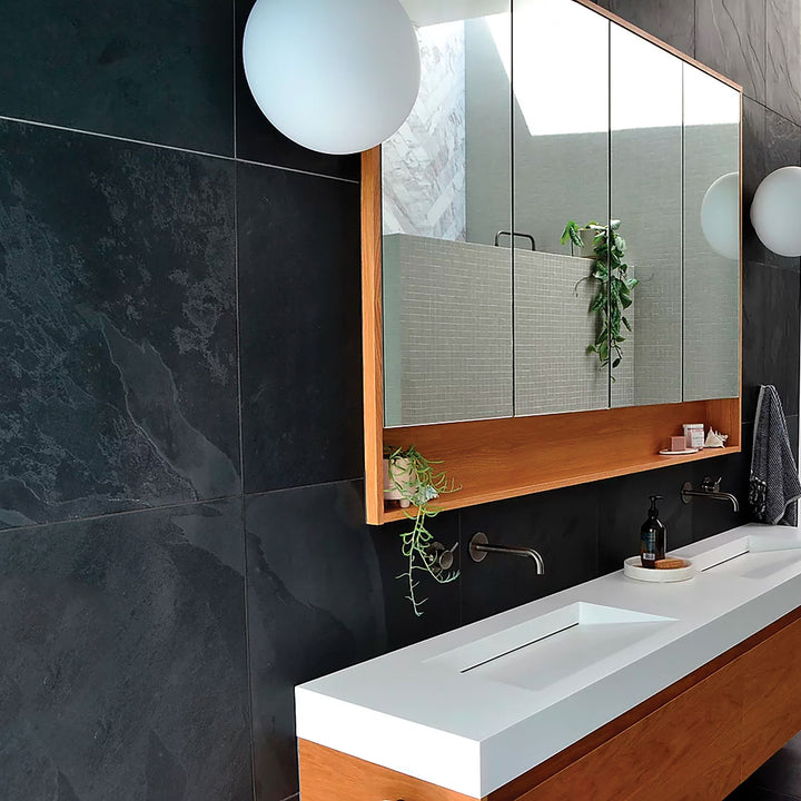 Modern bathroom with dark tiled walls, a white sink, and a large mirror.